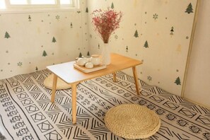 A room with a patterned floor, a small wooden table with a vase and teapots, and a woven stool. - Snowlake-Inn (Shangri-La)