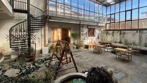 Un amplio espacio interior con una escalera espiral, un área diáfana con mesas y sillas, y una estructura tipo invernadero con paredes de vidrio.