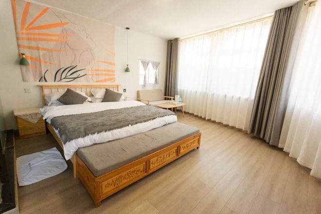 A bedroom with a large bed, a bench, a nightstand, a lamp, and a window with curtains.
