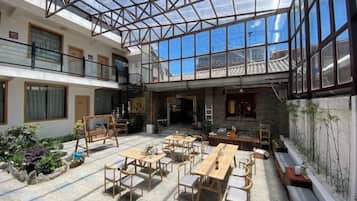 A spacious indoor area with multiple wooden tables and benches, a glass ceiling, and a view of the outside.