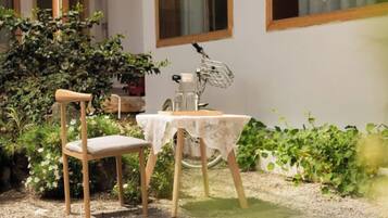 Un juego de mesa y silla de madera sobre grava, con una planta en maceta y una ventana al fondo.