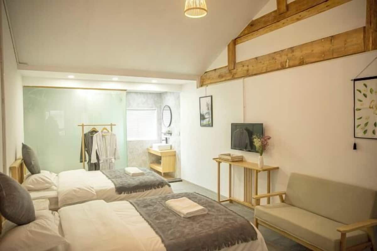 A bedroom with two beds, a wooden ceiling, a small table with a vase, and a chair.