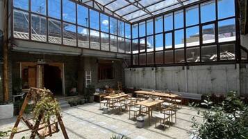A greenhouse-style room with tables and chairs, large windows, and plants.