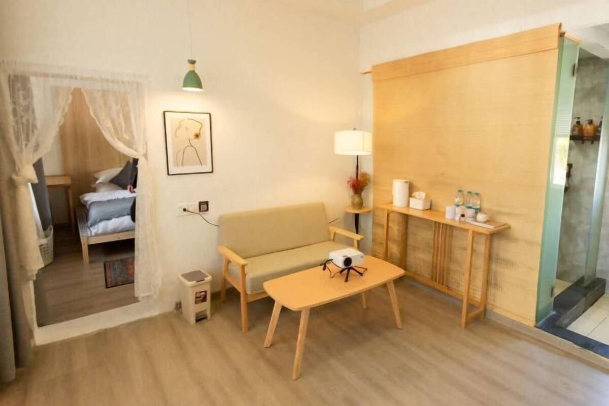 A hotel room with a bed, a sofa, a small table, a lamp, and a wooden cabinet.