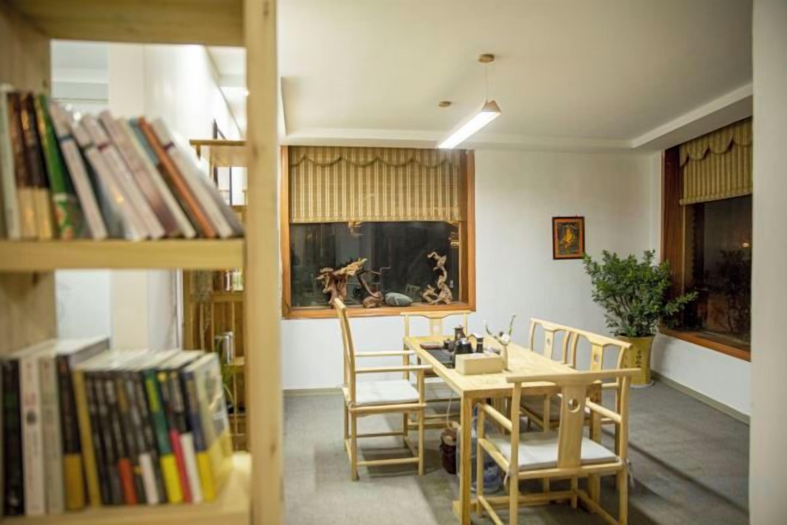 Una habitación con una mesa de comedor, sillas, una estantería, una ventana con cortinas y una planta.
