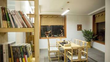 Una habitación con una mesa de comedor, sillas, una estantería, una ventana con cortinas y una planta.