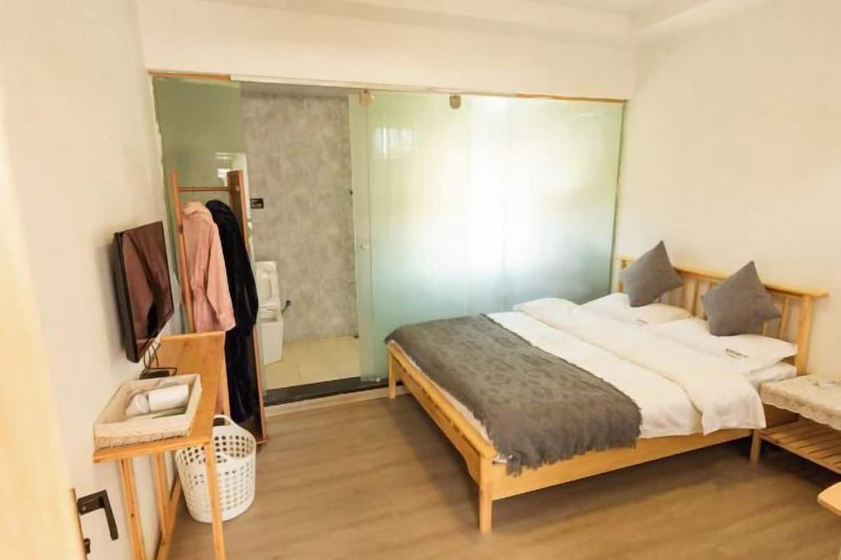 A bedroom with a bed, a wooden headboard, a bedside table, a mirror, a wardrobe, and a door leading to a bathroom.