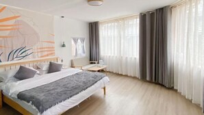 Un dormitorio con cama, escritorio, silla y una ventana grande con cortinas.