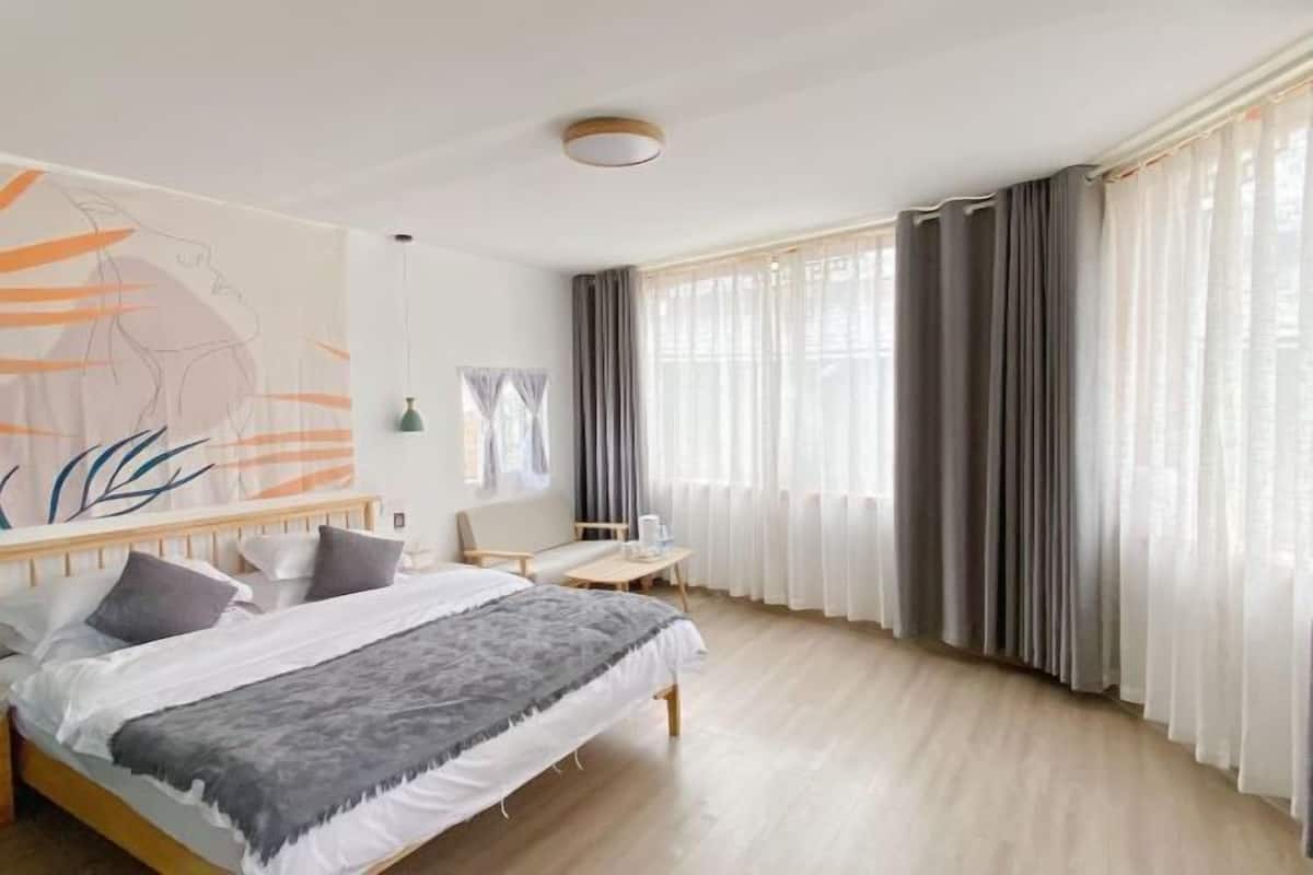 A bedroom with a bed, a desk, a chair, and a large window with curtains.