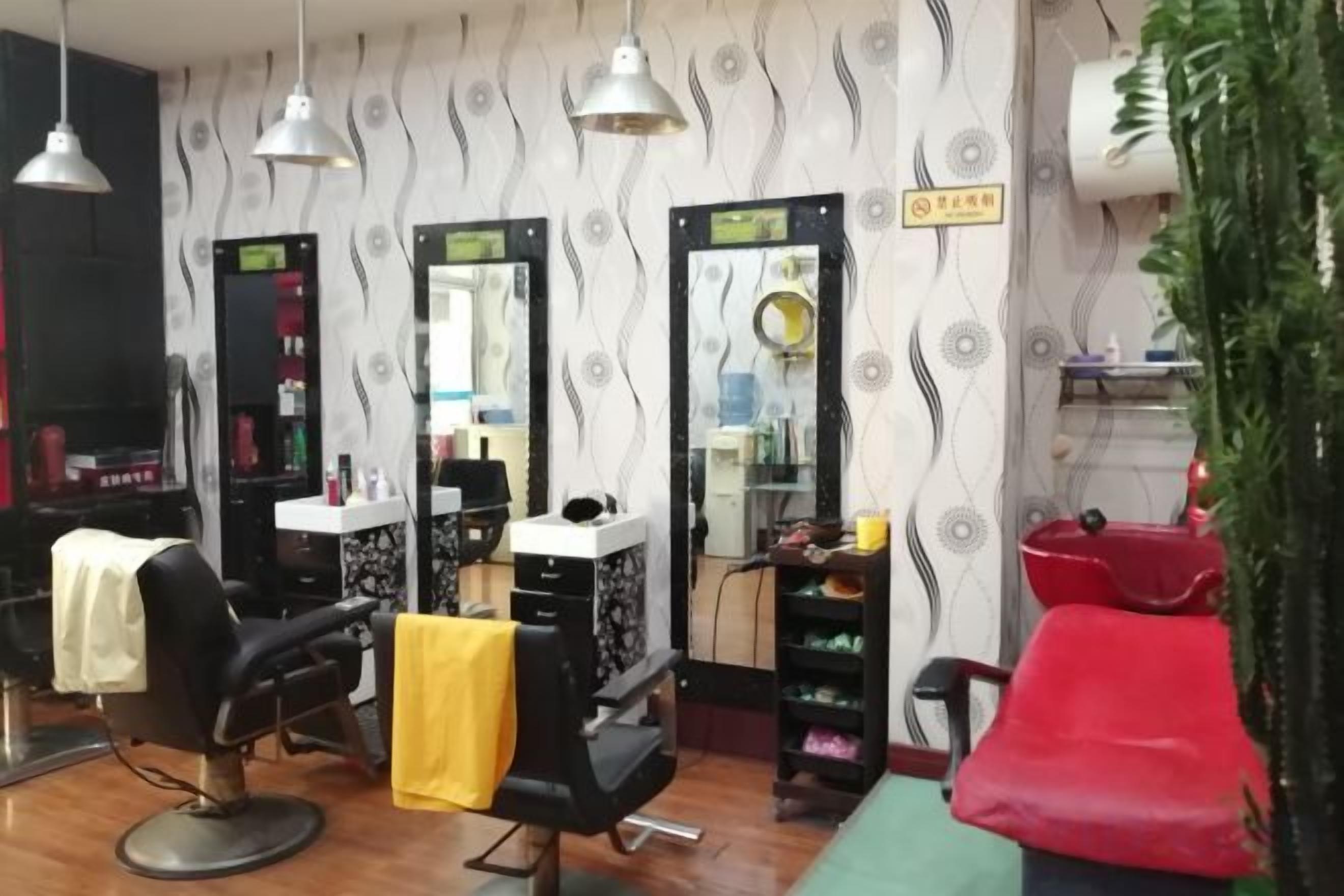 Un salón con varios espejos, una estación de lavado de cabello y una zona de espera con una silla roja.
