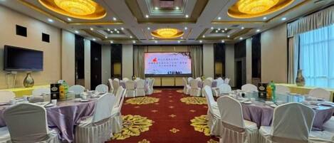 A conference room with round tables, chairs, a large screen, and a red carpet.