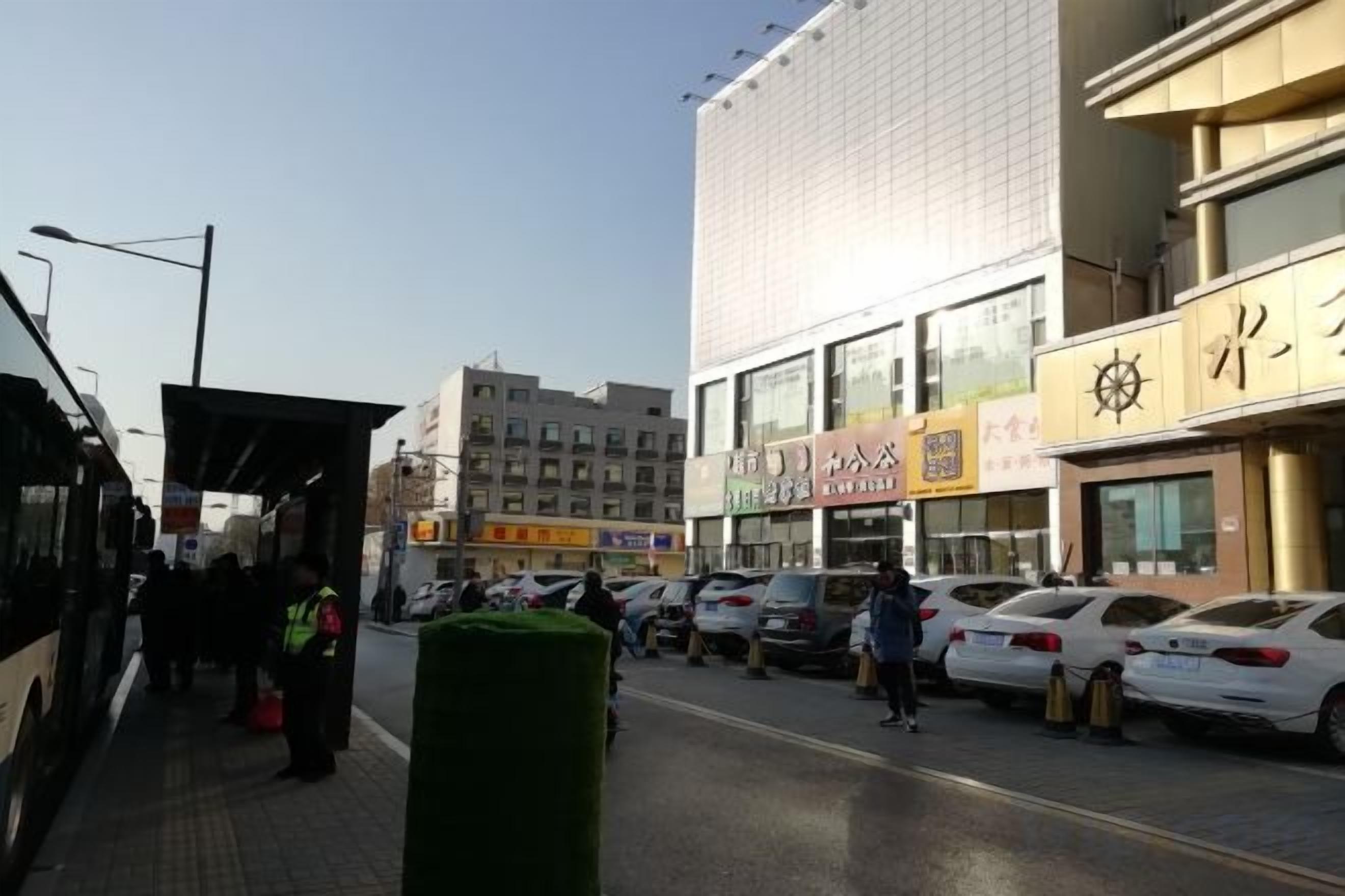 Una calle con autos estacionados, una parada de autobús y edificios con letreros comerciales.