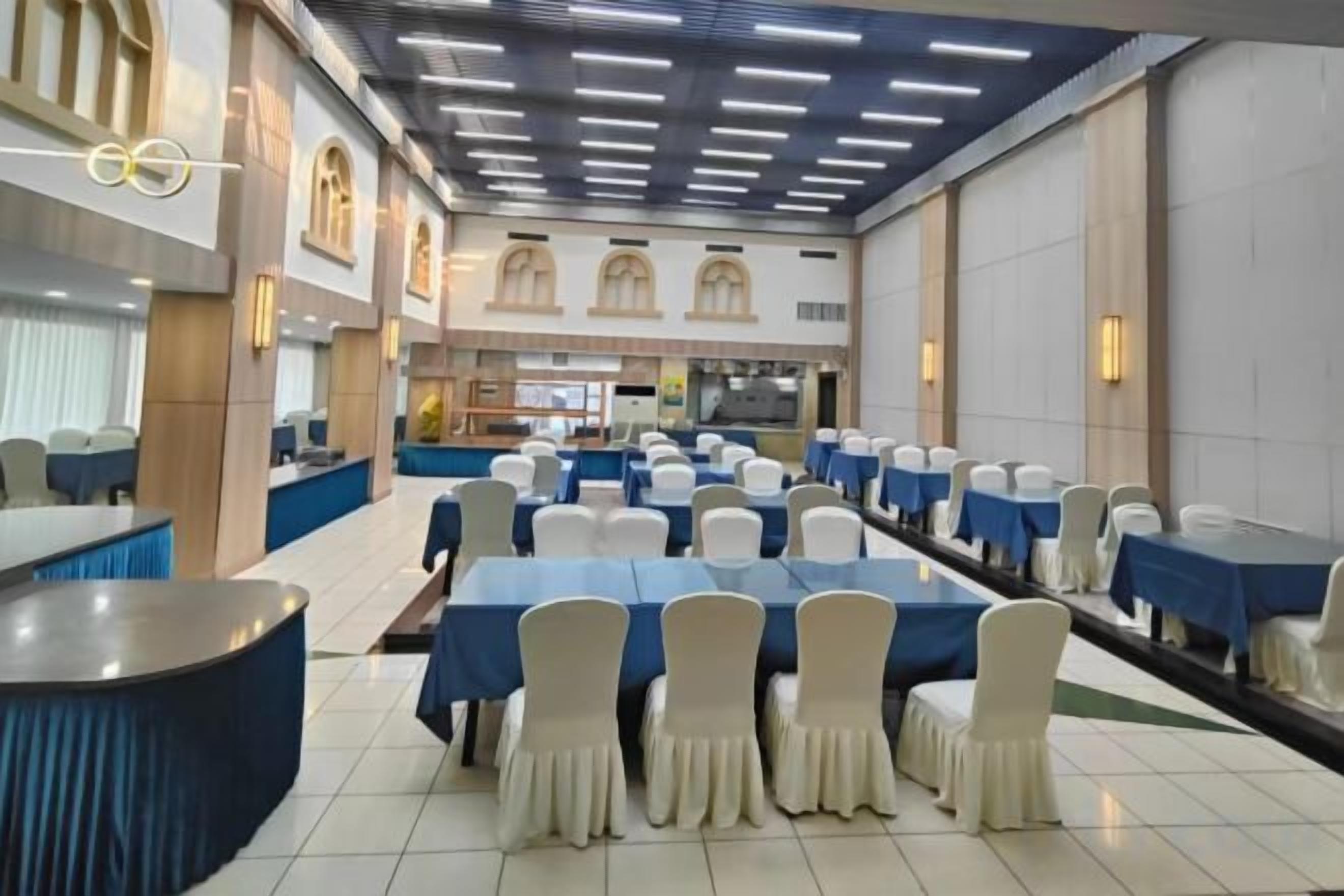 Un salón de banquetes con mesas dispuestas en filas, una barra y una zona de cocina al fondo.