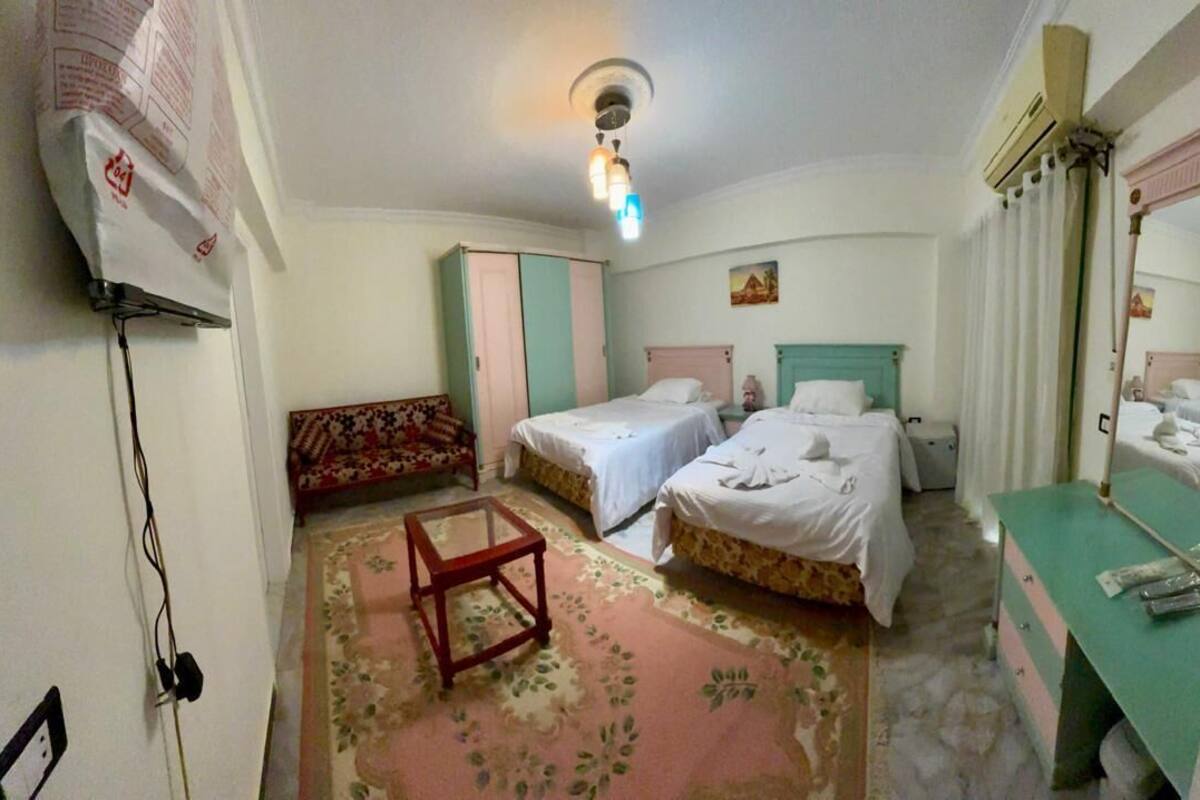 A hotel room with two beds, a small table, a sofa, and a bathroom with a mirror.