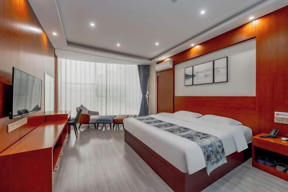 Habitació d'hotel amb llit, escriptori, cadira, televisió i finestra amb cortines.