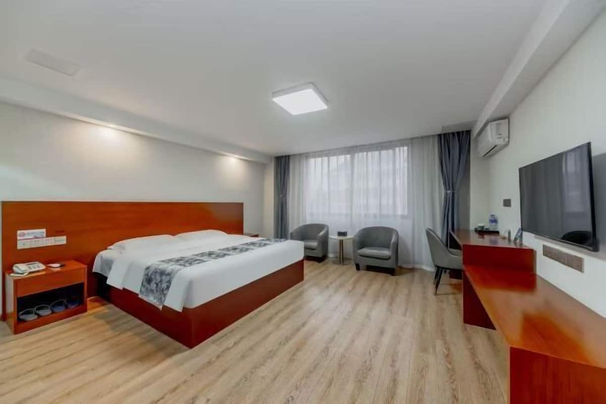 Habitació d'hotel amb llit de fusta, escriptori, dues cadires, televisió i finestra amb cortines.