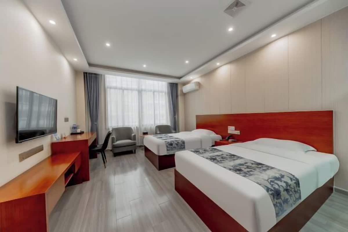 Una habitació d'hotel amb llit, escriptori, cadira, televisió i finestra amb cortines.