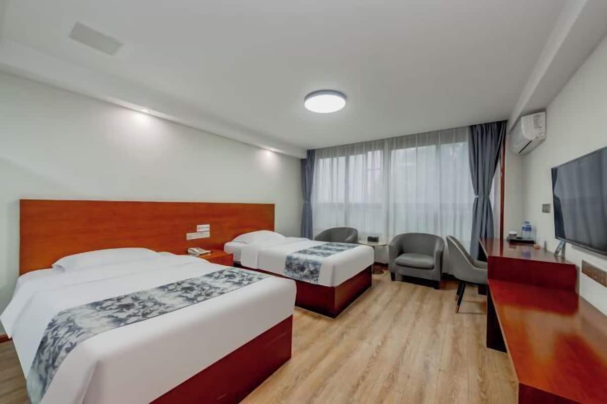 Habitació d'hotel amb dos llits, un escriptori, una cadira, una televisió i una finestra amb cortines.