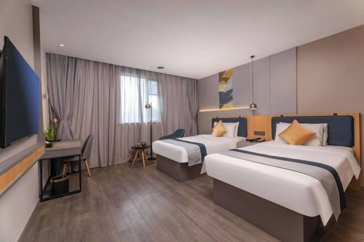 Habitación de hotel con dos camas, un escritorio, una silla, un televisor y una ventana con cortinas.