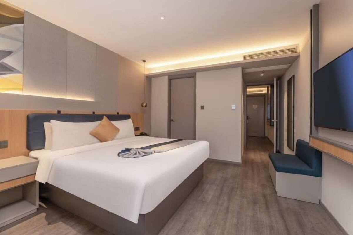 Una habitación de hotel moderna con cama, mesitas de noche, televisor y zona de estar.