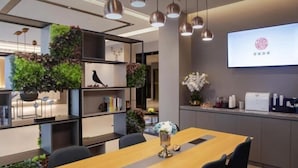 A modern office space with a long wooden table, black chairs, hanging pendant lights, and a projector screen displaying a logo. - Homeinn Selected Hotel (Suzhou North Railway Station Cailian Plaza) (Suzhou)