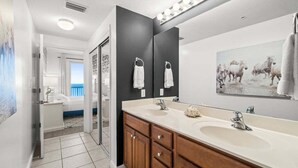 A modern bathroom with two sinks, wooden cabinets, and a large mirror. - Fall Deals + Snowbird Rates | Gulf Front Beach Escape (Panama City Beach)