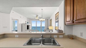 A modern kitchen with a double sink, wooden cabinets, and a view of the ocean. - Fall Deals + Snowbird Rates | Gulf Front Beach Escape (Panama City Beach)
