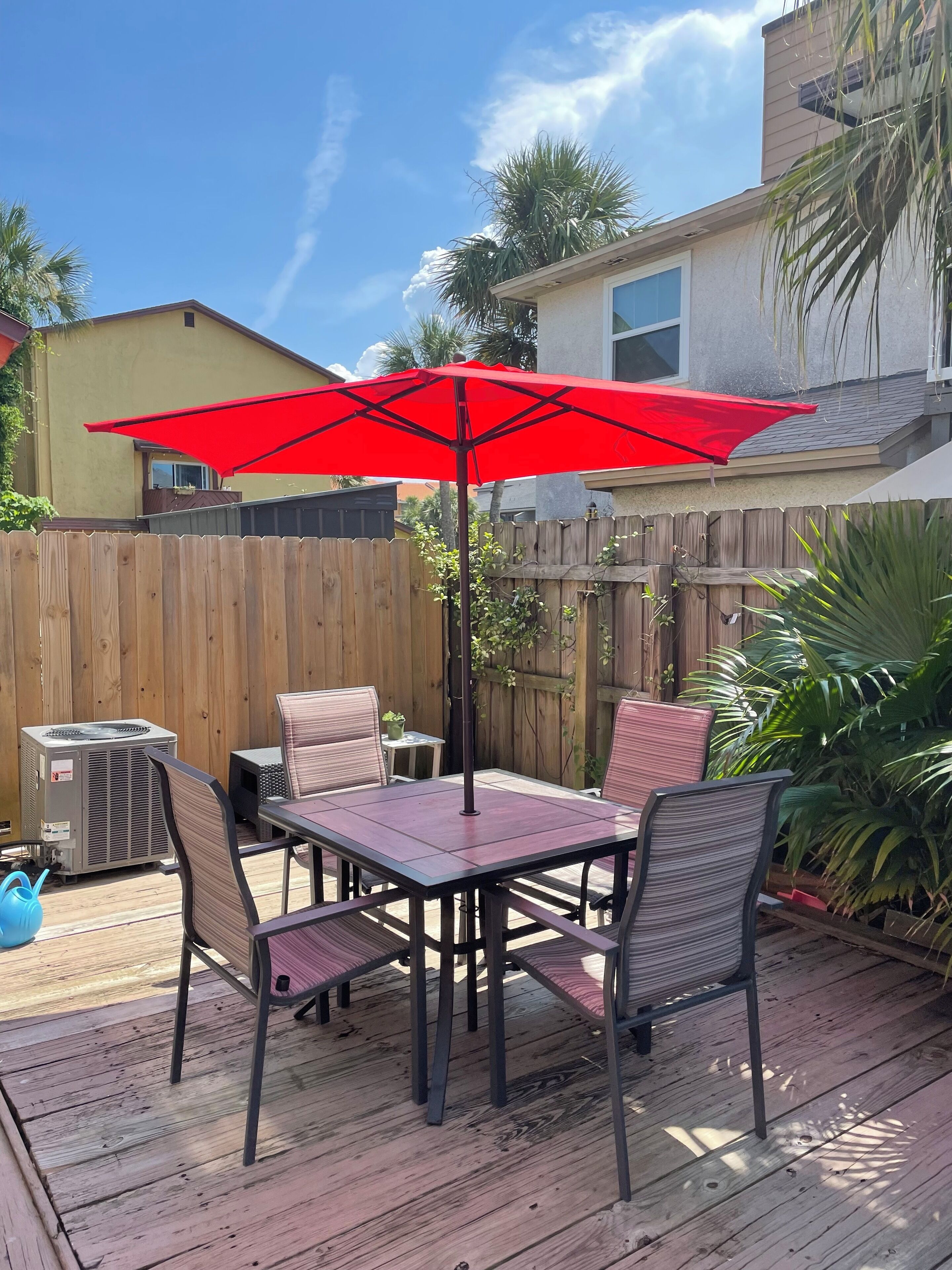 Une terrasse en bois avec une table et des chaises, un parasol rouge et un appareil de climatisation.