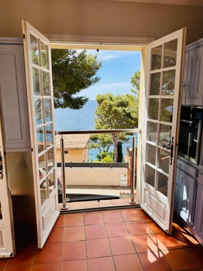 Ein offenes Durchgangsbild zu einem Balkon mit Blick auf das Meer und Bäume.