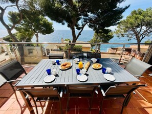 A table set for breakfast with a view of the sea, outdoor chairs, and a tiled floor. - Authentic family home "La Pinède" Sea view (Ensuès-la-Redonne)