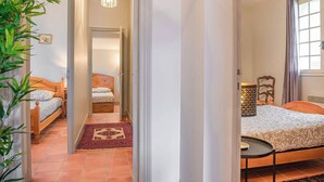 Ein Schlafzimmer mit Bett, Nachttisch, Lampe und Blick auf einen Flur.