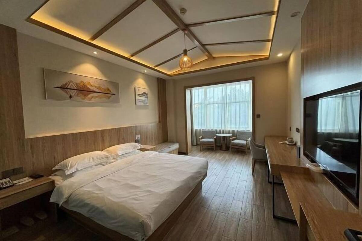 A modern hotel room with a large bed, a desk with a TV, a seating area, and artwork on the walls.