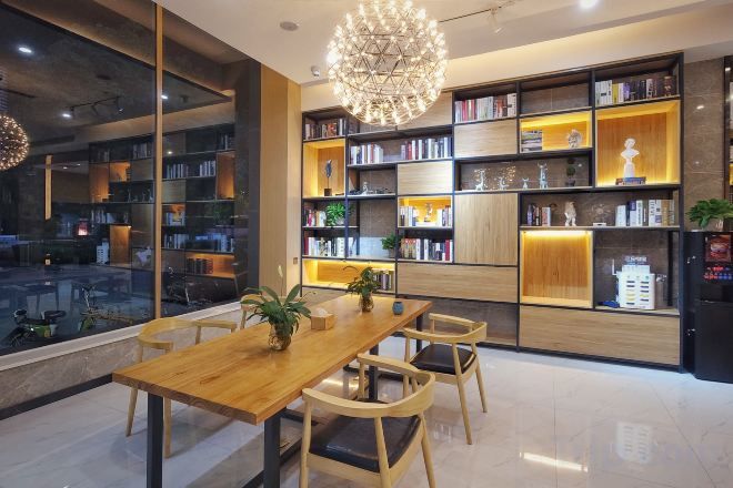 A modern interior with a wooden dining table, chairs, and a large bookshelf filled with books and decorative items.