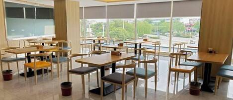 A modern dining area with tables and chairs, large windows, and a view of the outdoors.