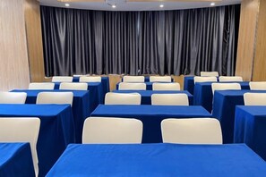 Un salón de conferencias con filas de mesas y sillas, un gran telón de fondo y una pared revestida de madera.