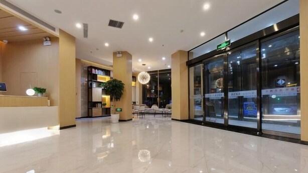 Un vestíbulo de hotel con piso de mármol pulido, una recepción, una planta grande en maceta y puerta de vidrio.