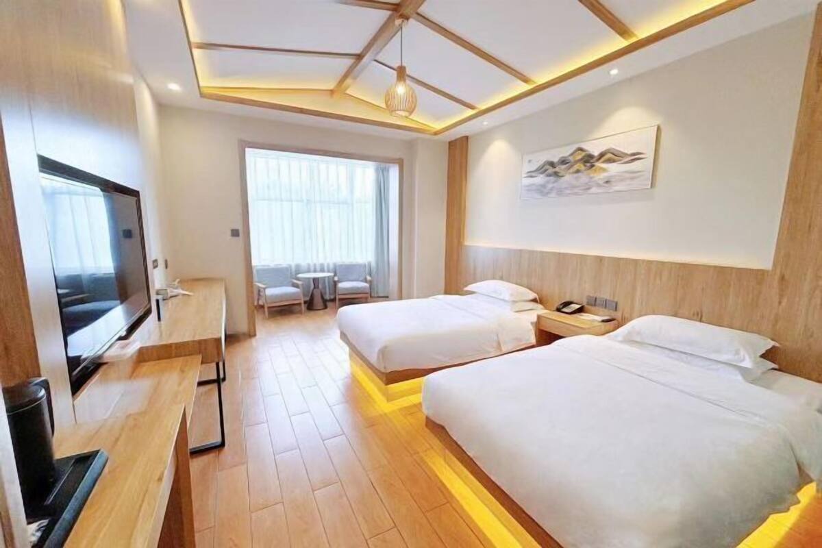 A hotel room with two beds, a TV, a desk, and a large window.