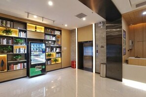 A modern hotel lobby with a vending machine, bookshelves, a reception desk, and a large mirror. - Lizun Select Hotel (Hebi Liyang Road Branch) (Hebi)