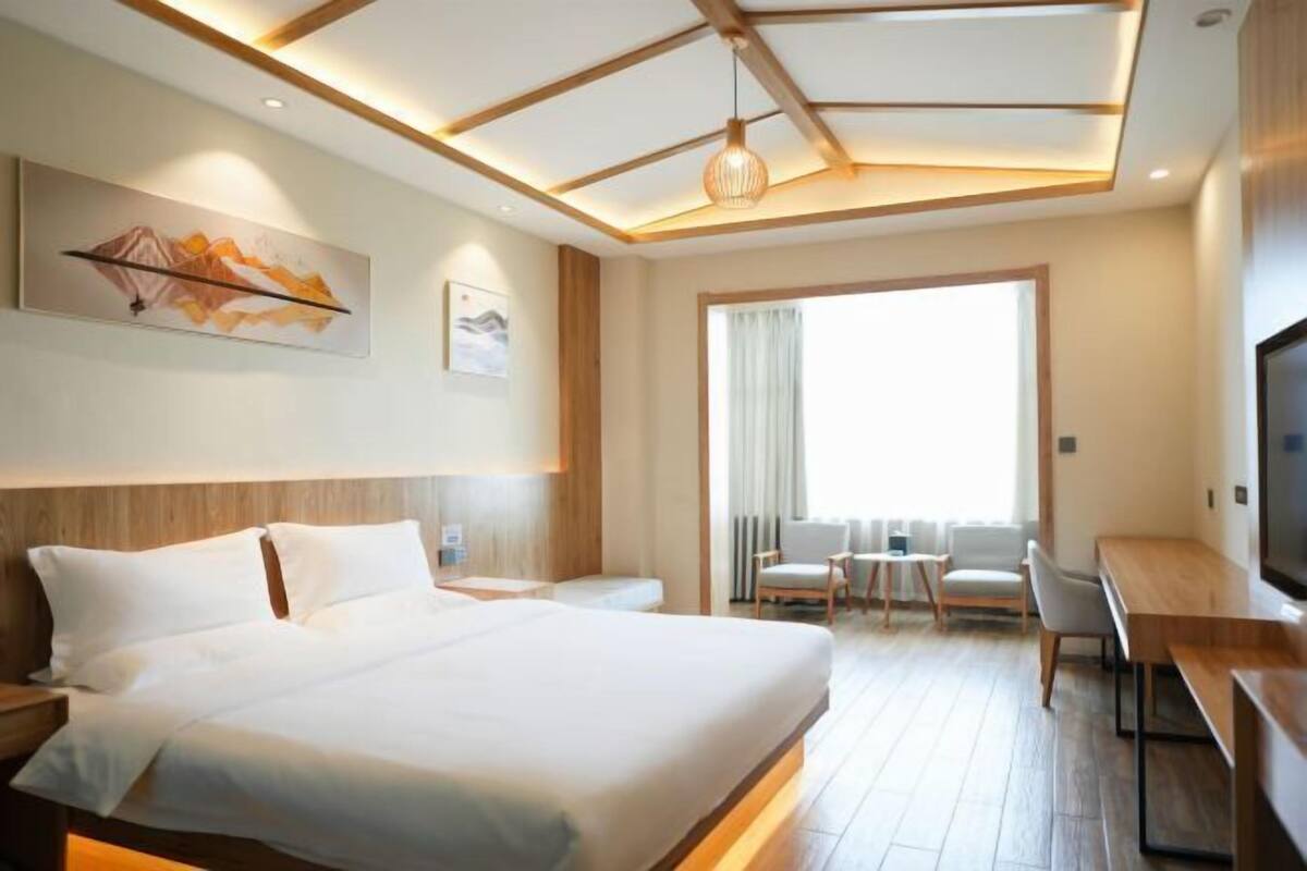 A hotel room with a large bed, a desk, a TV, and a balcony with a view.