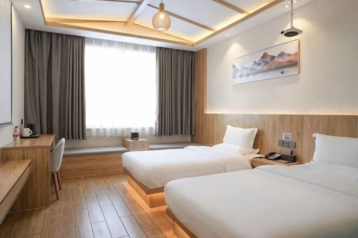 A hotel room with two beds, a desk, a chair, a window with curtains, and a painting on the wall.