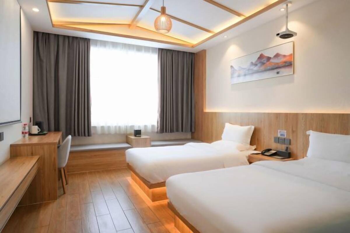 A hotel room with two beds, a desk, a chair, a small table, and a painting on the wall.