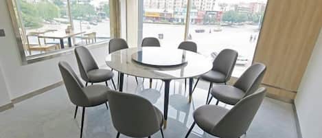 A conference room with a round table and eight chairs, large windows with blinds, and a view of the cityscape.