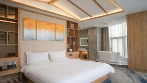 Una habitación de hotel moderna con una cama grande, estanterías integradas, un tocador con espejo, una bañera y un ventanal amplio.