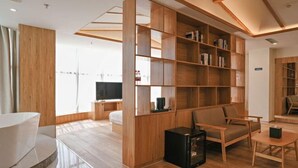 Una habitación de hotel moderna con una estantería de madera, un sofá, una mesa de centro y un televisor.