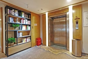 Un hall de hotel con una estantería de madera, un ascensor y un contenedor de basura.