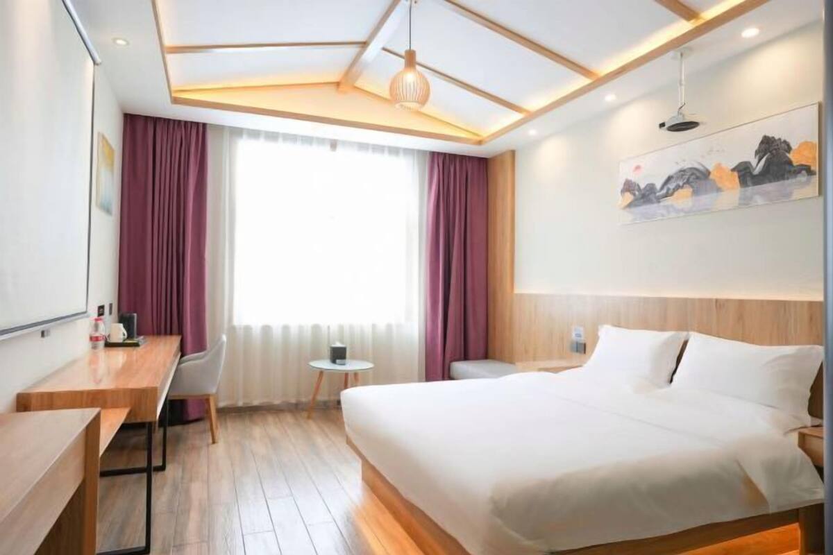 A hotel room with a bed, a desk, a chair, a small table, and a painting on the wall.
