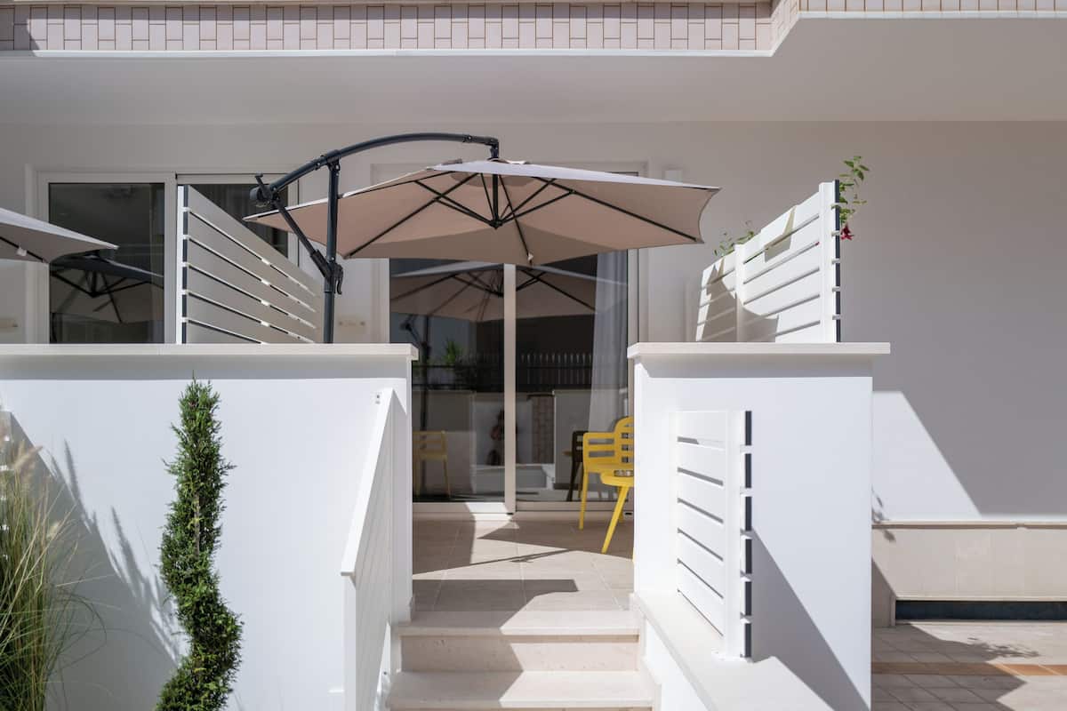 A staircase leading to a covered outdoor area with a table and chairs, a large umbrella, and a small plant.