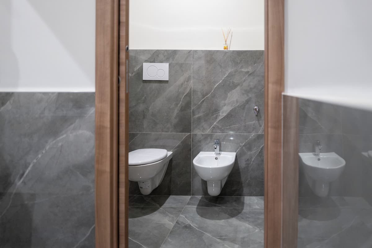 A modern bathroom with a toilet, bidet, and sink, all with marble walls and wooden accents.