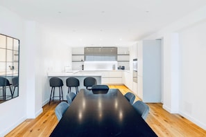 A modern kitchen with white cabinets, a central island, and bar stools. - Iconic Family Home: 3BR | 3.5BA | Sleeps 10 (London)