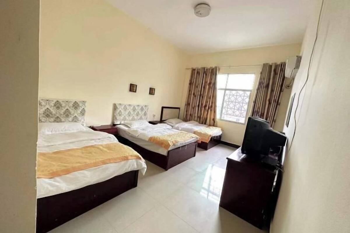 Quarto de hotel com três camas, televisão e janela com cortinas.